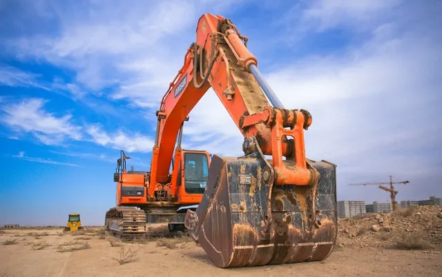 An orange excavator with its bucket lowered on a dirt construction site under a blue sky