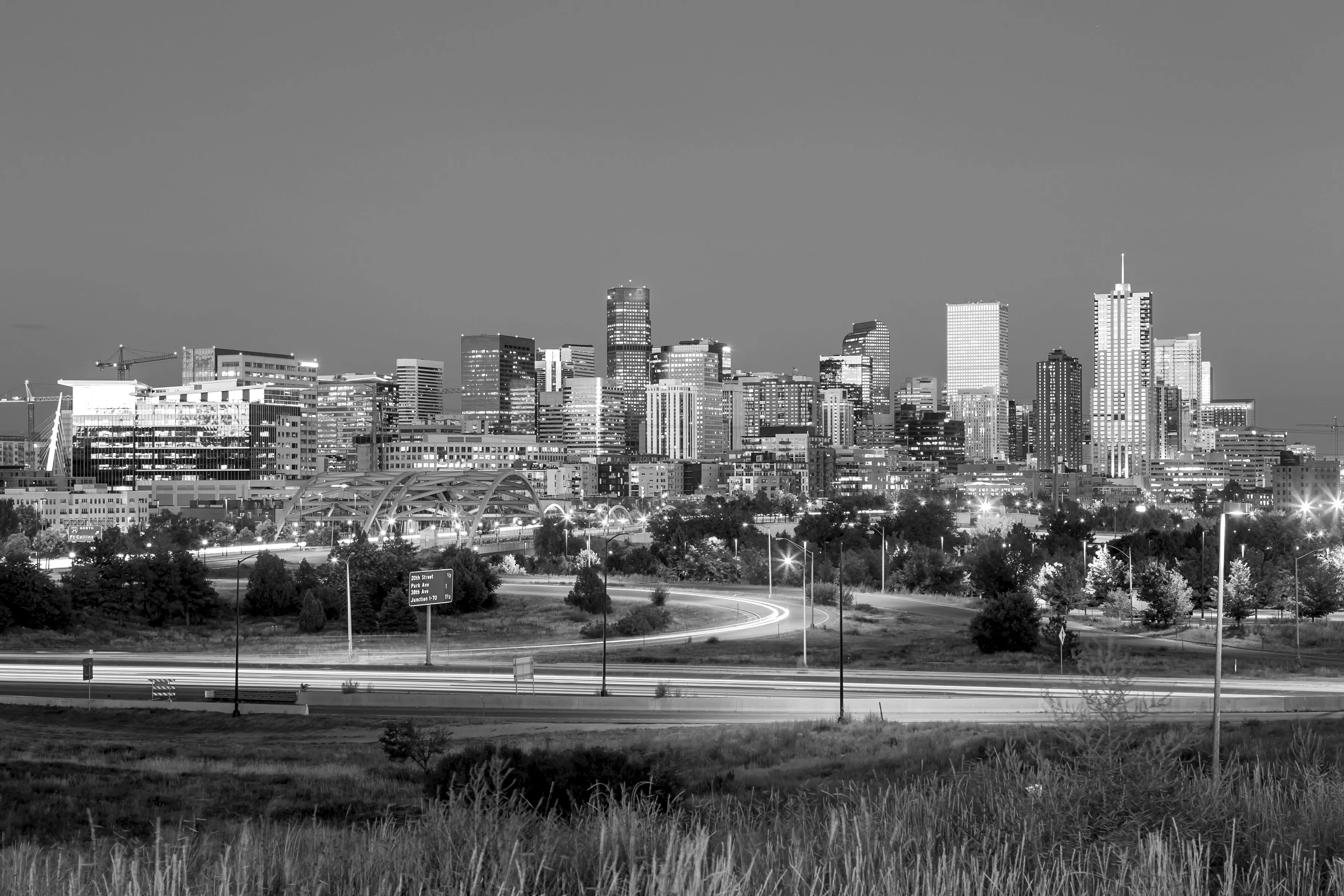 Black-and-white view of the downtown Denver skyline at night, with light trails on the highway in the foreground