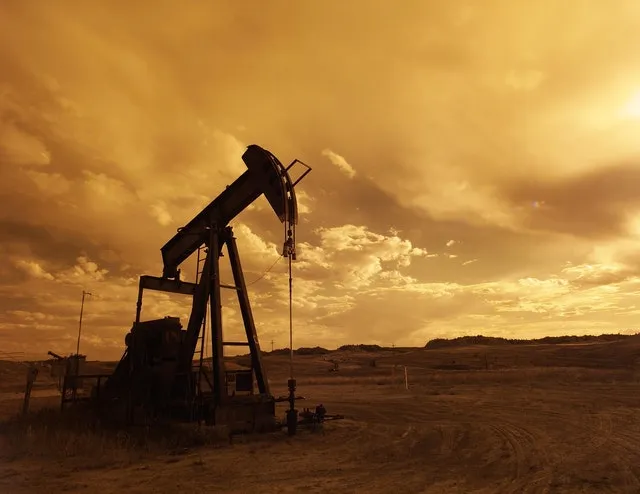 Silhouette of an oil pump jack in an open field under a golden, cloudy sky