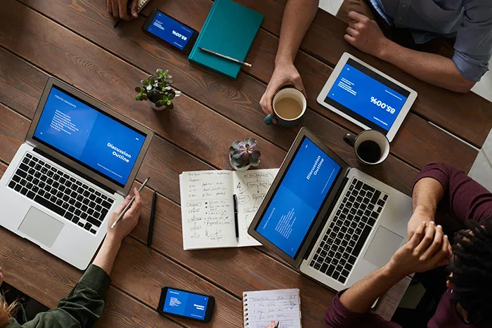 Overhead view of colleagues at a wooden table with laptops, tablets, notebooks and cups of coffee